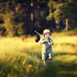 Mały chłopiec w dżinsowym kombinezonie i kapeluszu idzie przez łąkę, trzymając na kiju zawiniątko, z zamyśloną miną.