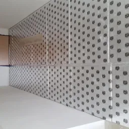 Ściana pokryta płytami z nadrukowanym wzorem, częściowo zabezpieczonymi folią ochronną, w trakcie prac wykończeniowych.