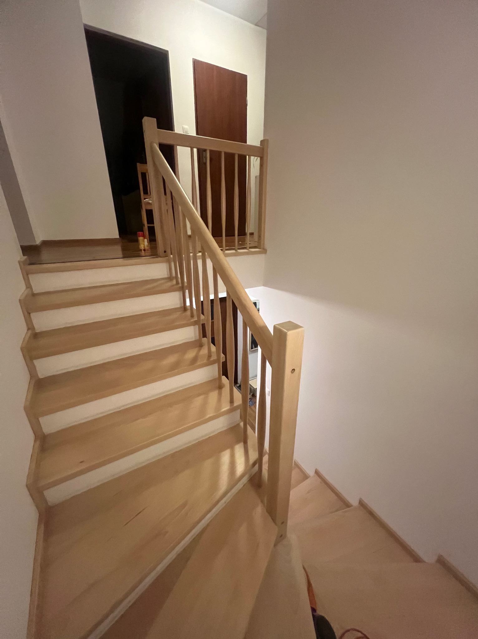 Jasne, drewniane schody z barierką w jasnym wnętrzu; widok z góry na stopnie z białymi podstopnicami.