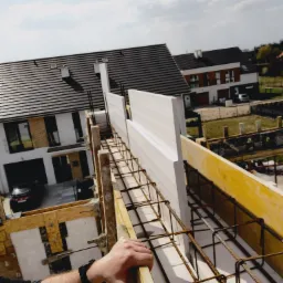 Budowa domu jednorodzinnego: szalunek zbrojeniowy z elementami styropianowymi, widok z góry na konstrukcję i okoliczne budynki.