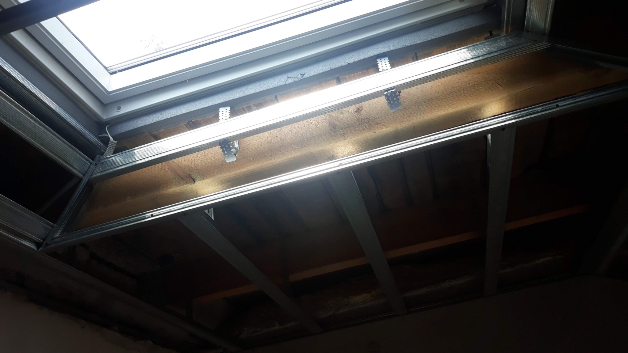 Metalowa konstrukcja pod sufitem, widoczne elementy drewniane i okno dachowe, etap prac wykończeniowych.