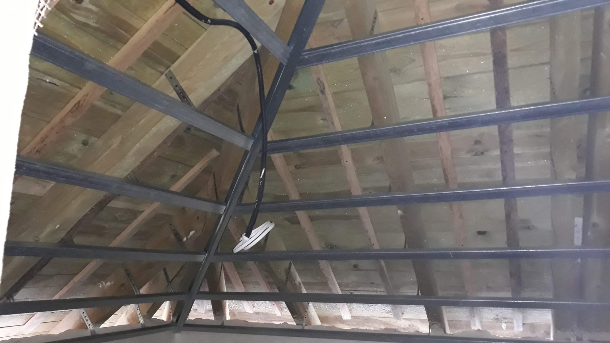 Konstrukcja metalowa podwieszana do drewnianego stropu, widoczne przewody elektryczne w peszlu, przygotowanie do montażu sufitu.