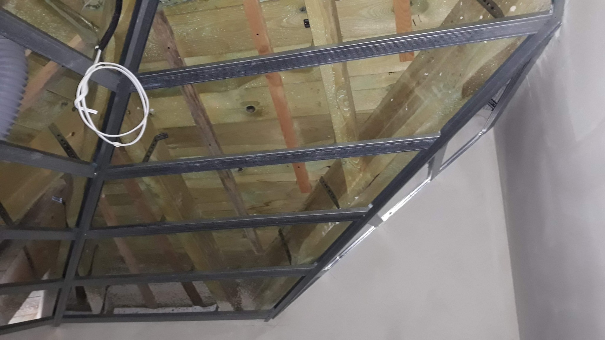 Metalowa konstrukcja sufitu podwieszanego z widoczną izolacją z wełny mineralnej i elementami instalacji elektrycznej w trakcie montażu.