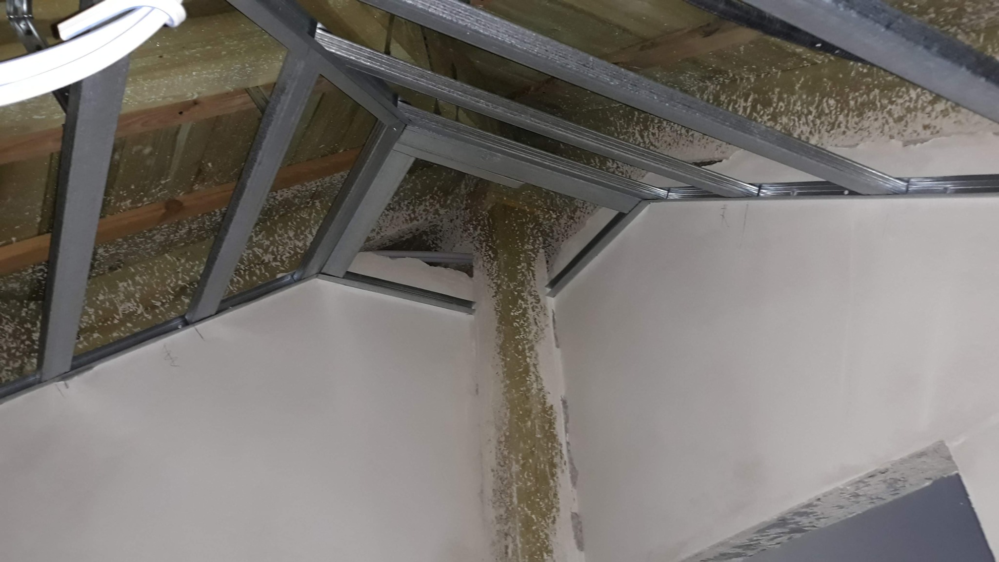 Konstrukcja metalowa podwieszanego sufitu z widoczną izolacją na drewnianym stropie i częściowo wykończoną ścianą z widocznymi śladami po szpachlowaniu.