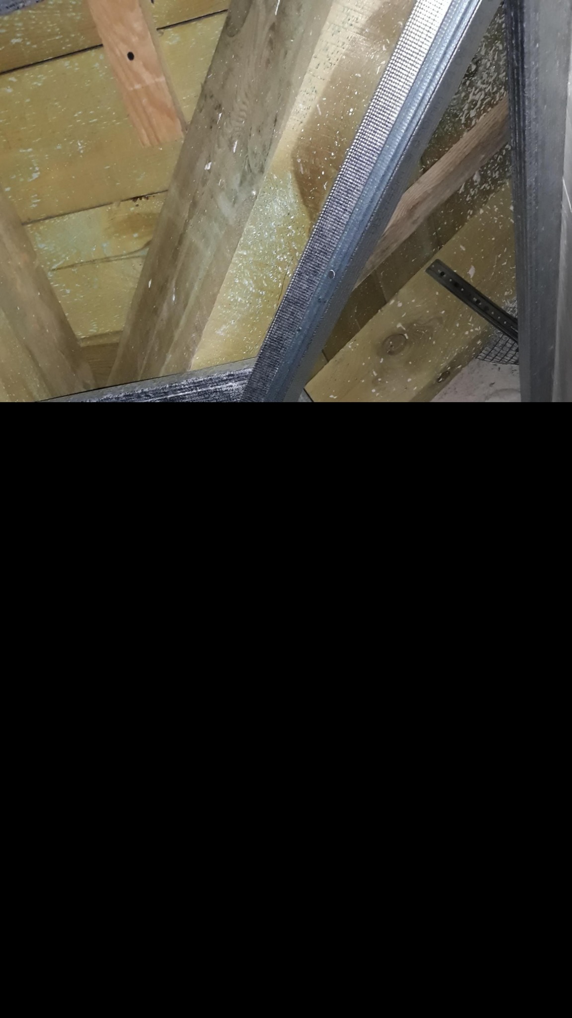 Metalowy stelaż sufitu podwieszanego, zamocowany do drewnianej konstrukcji stropu, widoczny od dołu pod kątem.