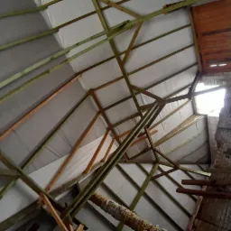 Wnętrze dachu w trakcie budowy z widoczną konstrukcją drewnianą, izolacją i fragmentem murowanego komina z uszkodzeniami.