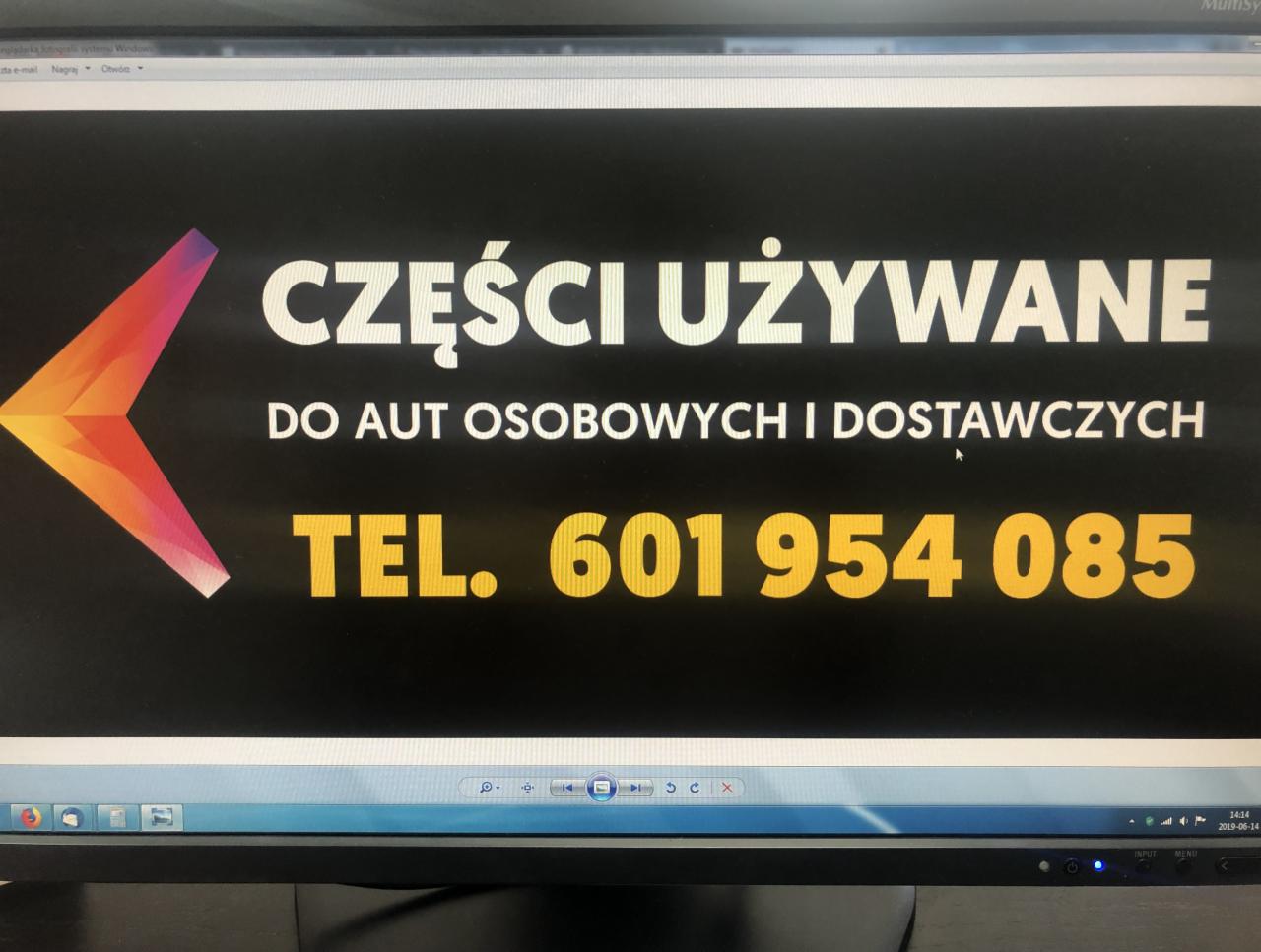 Ogłoszenie na ekranie monitora: 'Części używane do aut osobowych i dostawczych. Tel. 601 954 085', z logo w kształcie strzałki w lewym górnym rogu.