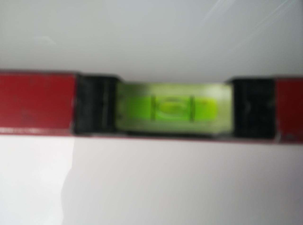 Poziomica z pęcherzykiem powietrza, ustawiona na świeżo pomalowanej, białej ścianie. Czerwona obudowa poziomicy. Bliskie ujęcie, wskazujące na dokładność wykonanej pracy.