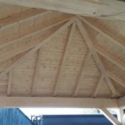 Drewniana konstrukcja dachu altany z widocznymi belkami i deskami, surowe drewno bez wykończenia, widok z dołu na konstrukcję szkieletową.