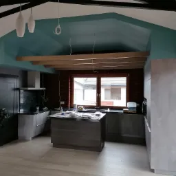 Nowoczesna kuchnia w szarościach z wyspą, ceglaną ścianą i turkusowym sufitem podczas montażu oświetlenia.