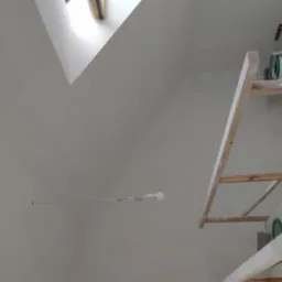 Świeżo pomalowane na biało poddasze ze świetlikiem, widoczne ślady po taśmie malarskiej, rusztowanie z narzędziami malarskimi i puszkami farb.