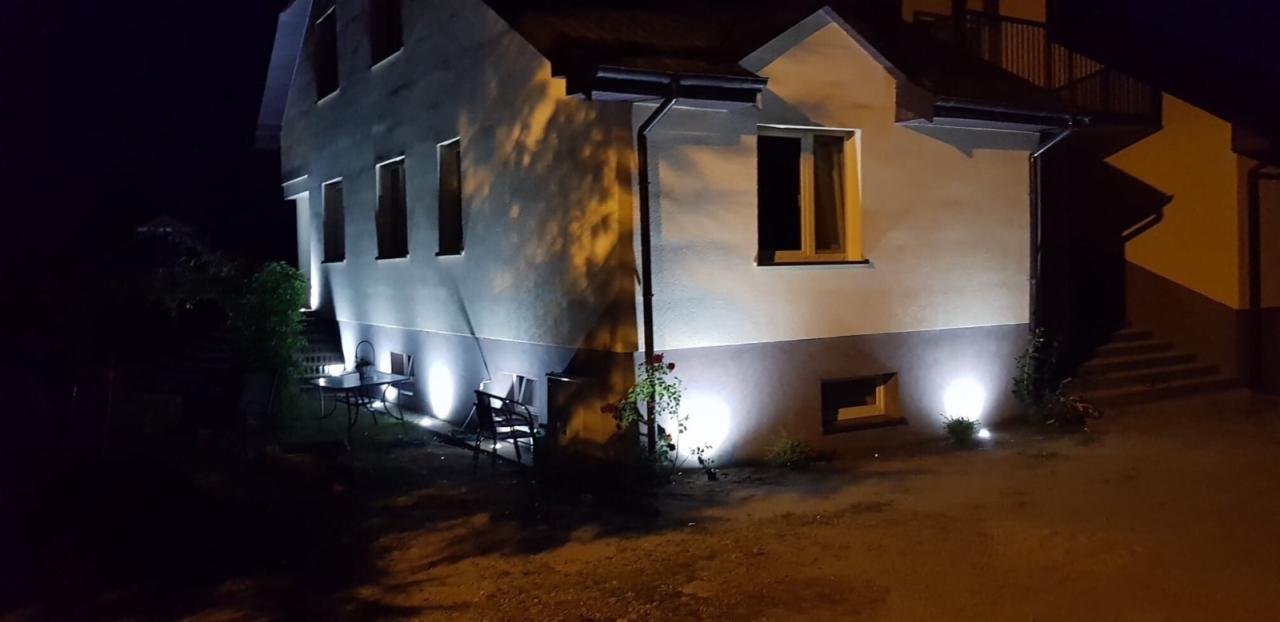 Nocne oświetlenie elewacji domu jednorodzinnego z lampami punktowymi LED, oświetlającymi także ogród i meble ogrodowe.