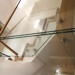 Nowoczesne schody z drewnianymi stopniami i szklaną balustradą mocowaną na metalowych wspornikach, widok od dołu.