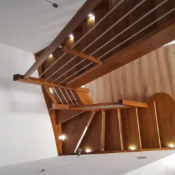 Nowoczesne schody z drewna z oświetleniem LED wbudowanym w konstrukcję, widoczne białe ściany i drewniana boazeria z zaokrąglonym wycięciem.