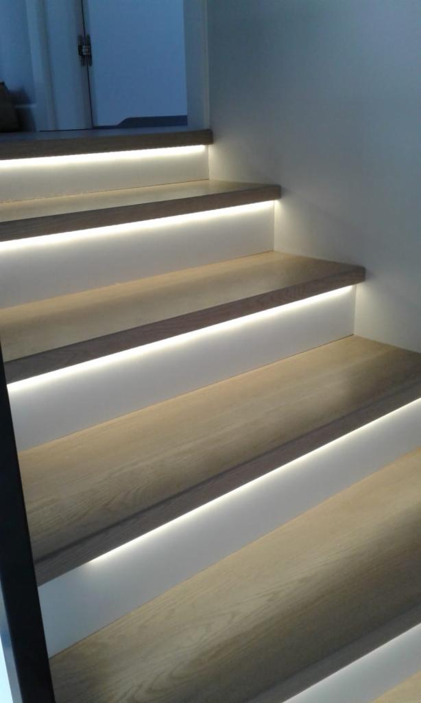 Nowoczesne schody drewniane z podświetleniem LED, ciepłe białe światło podkreśla strukturę drewna, minimalistyczny design.