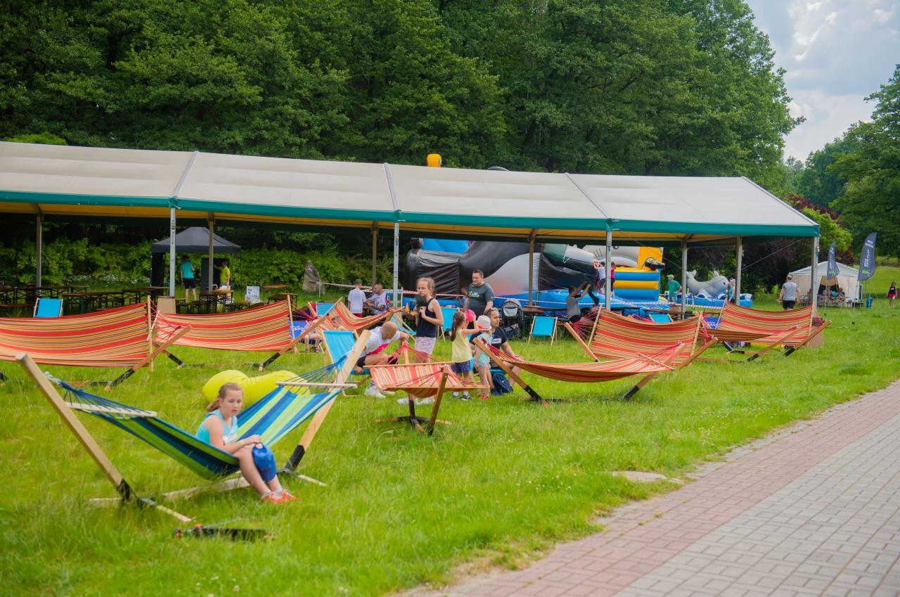 Plenerowa strefa relaksu z hamakami i dmuchanym zamkiem podczas imprezy na trawie.