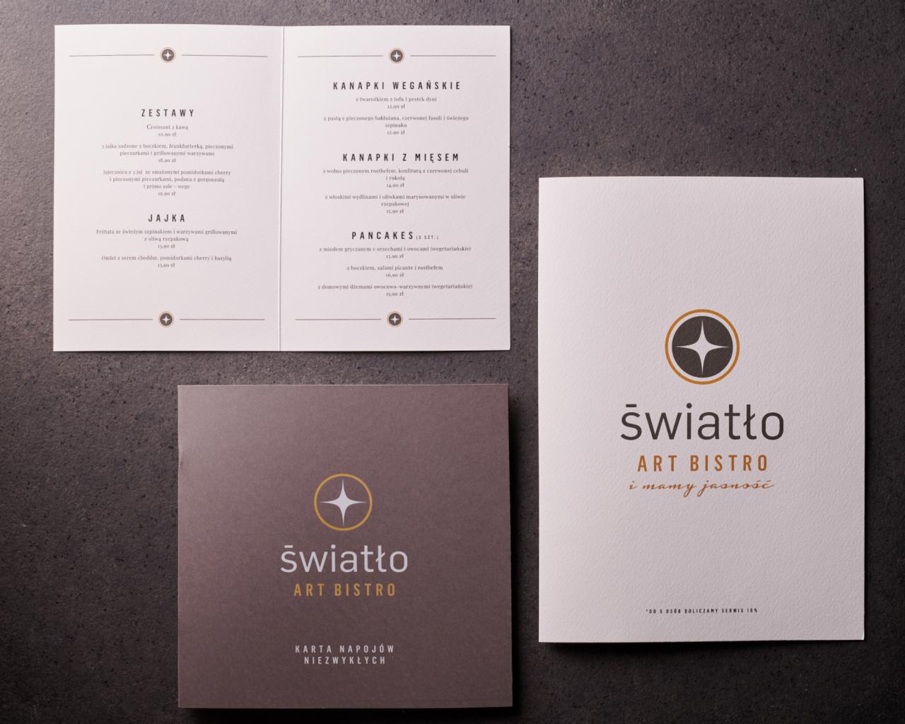 Trzy karty menu restauracji Art Bistro 'Światło' na ciemnym tle, prezentujące ofertę śniadaniową i napojów, z wyraźnym logo i hasłem 'i mamy jasność'.