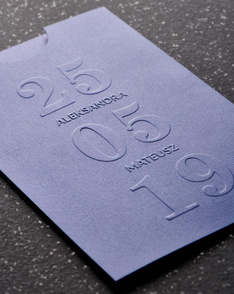 Elegancka, fioletowa wizytówka z wytłoczonymi imionami Aleksandra i Mateusz oraz datą ślubu 25.05.2019 na teksturowanym tle.