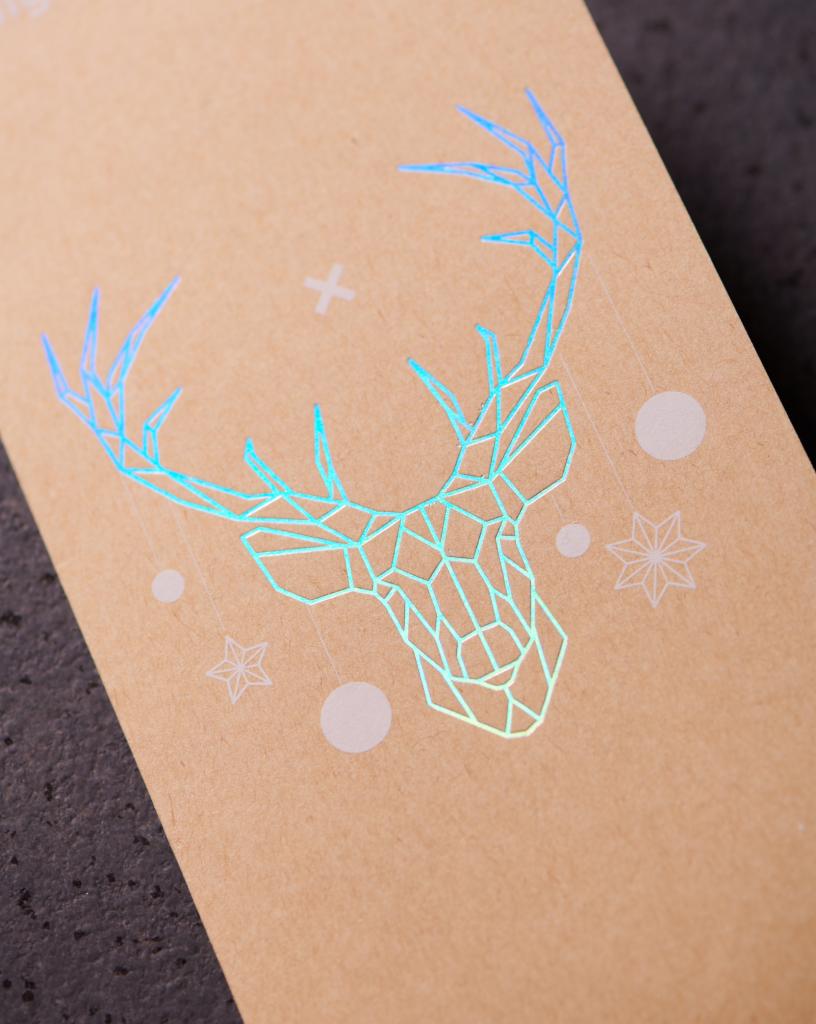 Kartonowa powierzchnia z holograficznym nadrukiem geometrycznego renifera i świątecznych symboli, widoczne pod kątem.