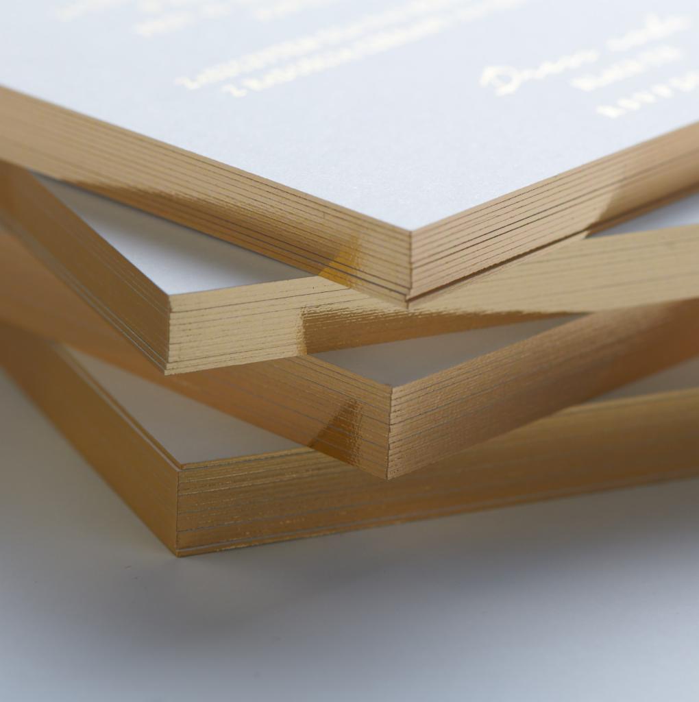 Stos wizytówek z białego papieru z pozłacanymi brzegami, ułożonych kaskadowo, widok z bliska na krawędzie.