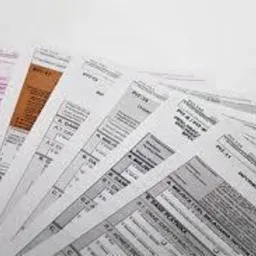 Stos dokumentów podatkowych VAT-7 i PIT-11 ułożonych wachlarzowo na białym tle, z widocznymi nagłówkami i tabelami.