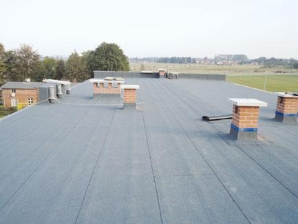 Wykończony, płaski dach pokryty papą termozgrzewalną z kominami wentylacyjnymi i ceglanymi kominami w Radzyminie.
