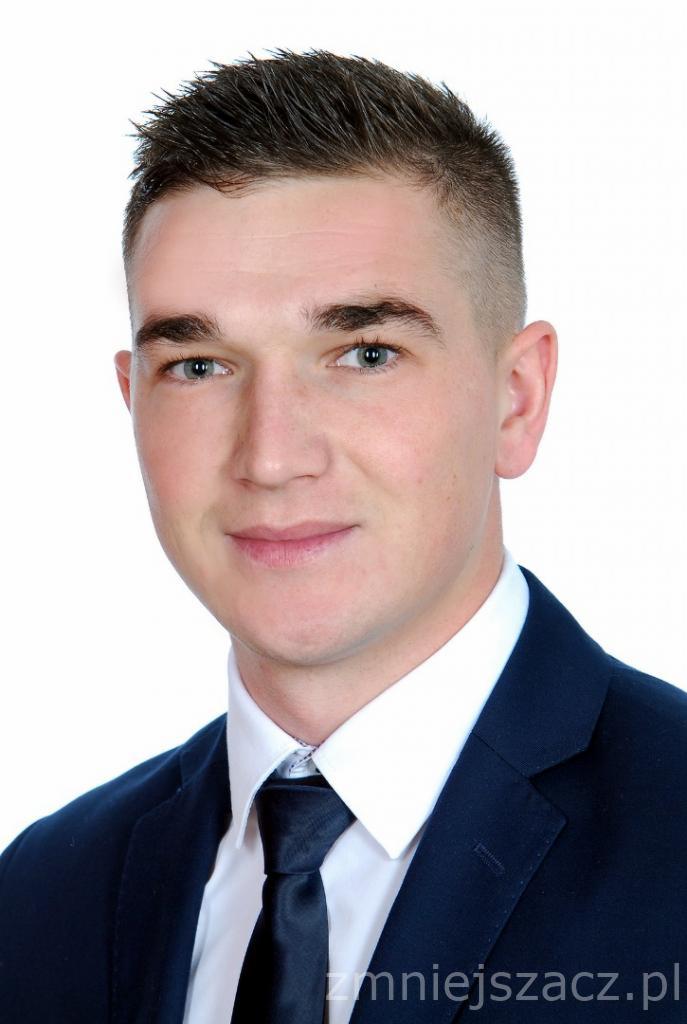 Portret młodego mężczyzny w granatowym garniturze i czarnym krawacie, z krótkimi włosami i jasną cerą, na białym tle. Zdjęcie studyjne.