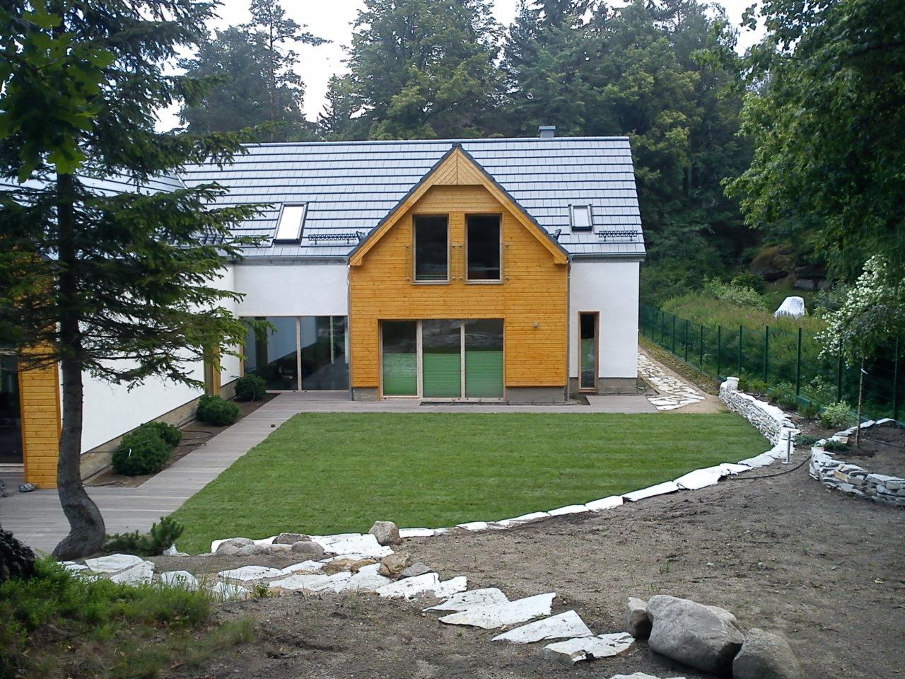 Nowoczesny dom z drewnianą elewacją i zadbanym trawnikiem, widok z perspektywy ogrodu z elementami kamiennego murku i ścieżki z płyt.