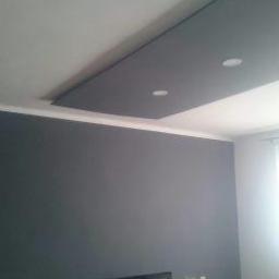 Remonty Katowice - Pokój po malowaniu ścian na szaro i zabudowie sufitu z oświetleniem punktowym, z widoczną bawiącą się dziewczynką i telewizorem.