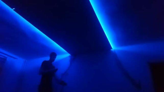 Wnętrze pokoju oświetlone niebieskimi, liniowymi lampami LED, z sylwetką osoby w tle.