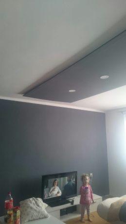 Pokój po malowaniu ścian na szaro i zabudowie sufitu z oświetleniem punktowym, z widoczną bawiącą się dziewczynką i telewizorem.