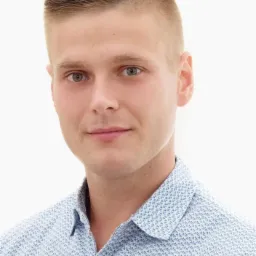 Portret młodego mężczyzny z krótkimi, zaczesanymi do góry włosami, ubranego w jasnoniebieską koszulę z drobnym wzorem.