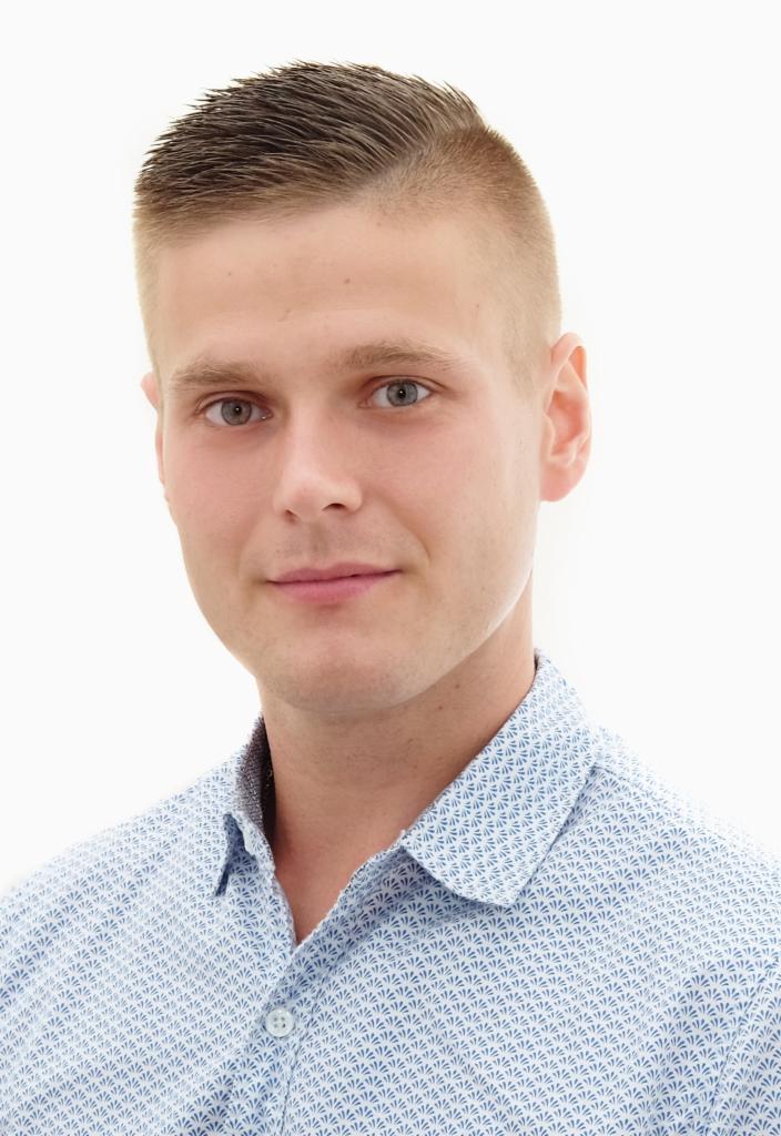 Portret młodego mężczyzny z krótkimi, zaczesanymi do góry włosami, ubranego w jasnoniebieską koszulę z drobnym wzorem.