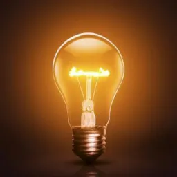 Świecąca żarówka z wyraźnie widocznym żarnikiem, oświetlona ciepłym, pomarańczowym światłem na ciemnym tle, z delikatnym odbiciem na powierzchni.