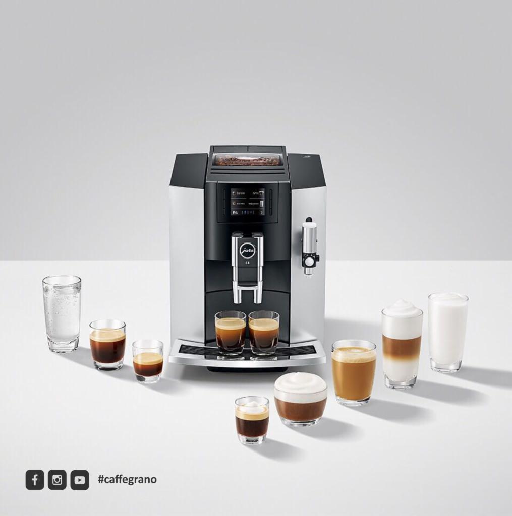 Automatyczny ekspres do kawy Jura E8 w kolorze srebrno-czarnym, prezentowany z różnymi rodzajami kaw w szklankach na białym tle, z widocznym logo #caffegrano w rogu.