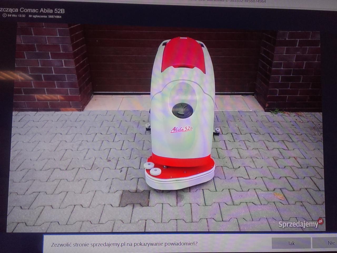 Profesjonalna maszyna czyszcząca Comac Abila 52B, stojąca na szarej kostce brukowej przed ceglanym budynkiem, widok z przodu.
