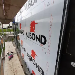 Montaż paneli elewacyjnych Alubond 9000 z użyciem przyssawek, widoczne rusztowanie i narzędzia na drewnianej desce.