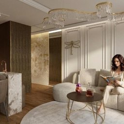 STUDIO INDYWIDUALNYCH INSPIRACJI ARTbis DESIGN Projekty Wnętrz i Elewacji Joanna Wal - Eleganckie wnętrze mieszkania w Krakowie: kobieta czyta książkę na sofie w salonie z aneksem kuchennym. Wystrój w odcieniach beżu, brązu i złota, z dekoracyjnym oświetleniem.