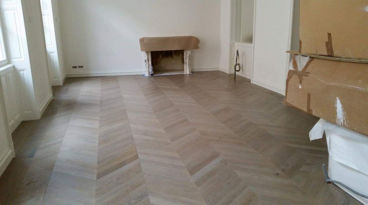 Nowo ułożony, jasny parkiet w jodełkę w pustym pokoju z zabezpieczonym kominkiem i kartonami w rogu.