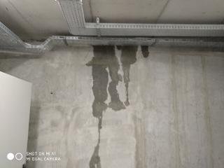 Przeciekająca instalacja elektryczna w korycie kablowym pod sufitem, widoczne zacieki na betonowej ścianie.