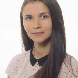 Portret kobiety z długimi, brązowymi włosami, ubranej w bluzkę w kropki z czarnym kołnierzykiem, na białym tle. Uśmiechnięta, patrzy wprost.