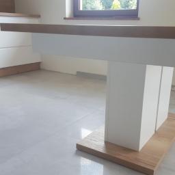 P.P.H.U WISAGE Sławomir Wierzbicki - Stół z drewnianym blatem i białymi nogami w nowoczesnej kuchni z białymi szafkami i szarą podłogą.