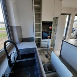 P.P.H.U WISAGE Sławomir Wierzbicki - Nowoczesna kuchnia z białymi szafkami, czarnym zlewem i baterią, wysuwanymi koszami na śmieci i systemami cargo, widok z bliska na zlew i kosze.