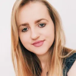 Portret uśmiechniętej blondynki z niebieskimi oczami na jasnym tle, z delikatnym makijażem i rozpuszczonymi włosami.