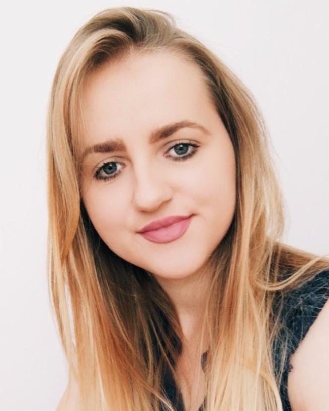 Portret uśmiechniętej blondynki z niebieskimi oczami na jasnym tle, z delikatnym makijażem i rozpuszczonymi włosami.