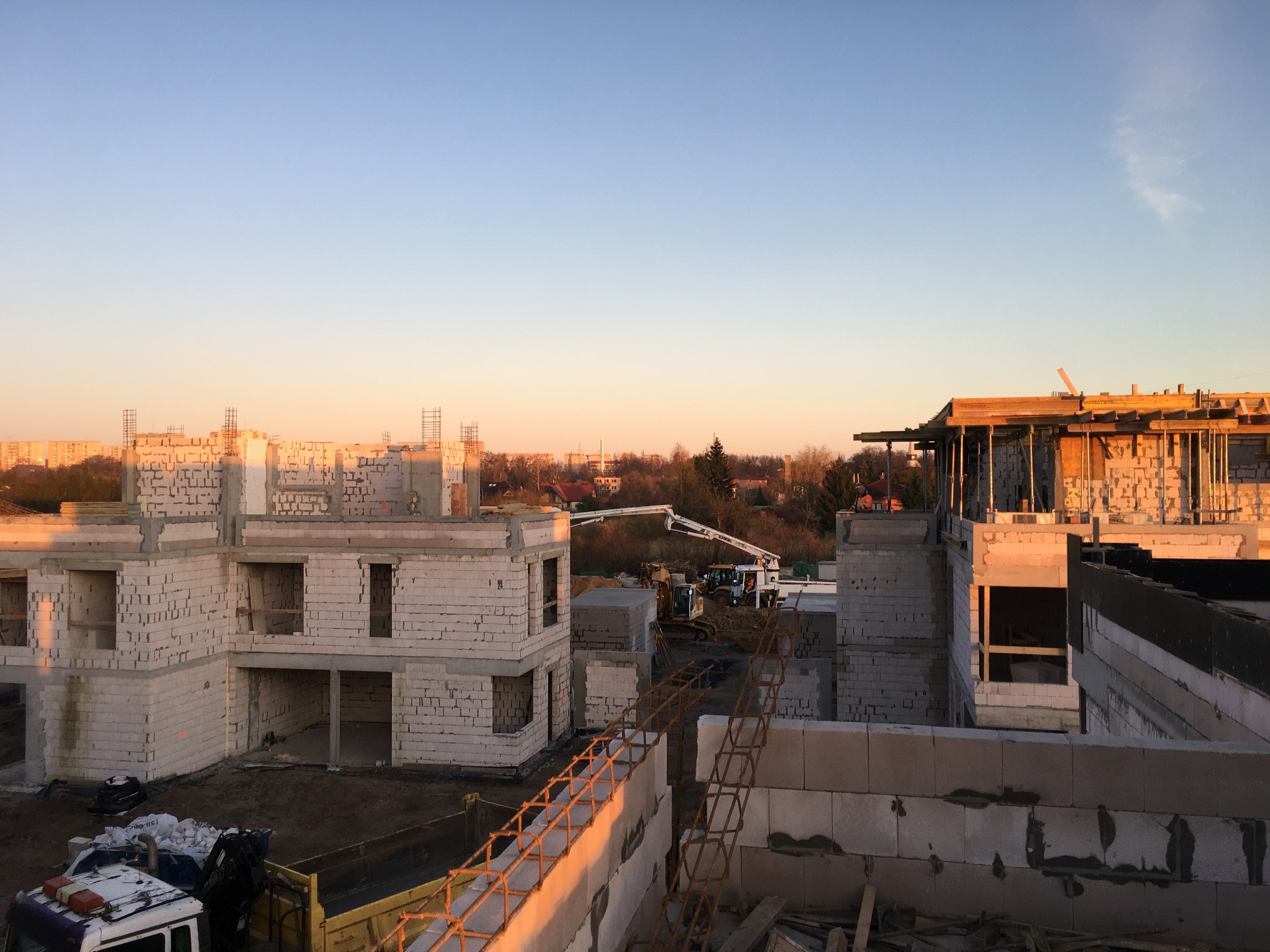 Budowa wielorodzinnego budynku z betonu komórkowego w trakcie wznoszenia, widoczna pompa do betonu i zbrojenie na pierwszym planie, ciepłe światło zachodzącego słońca.