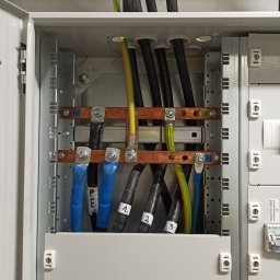 Usługi elektryczne - Wnętrze otwartej skrzynki rozdzielczej z grubymi kablami oznaczonymi numerami 1, 2, 3 oraz PE i PEN, podłączonymi do szyn zbiorczych z miedzianymi elementami i śrubami.