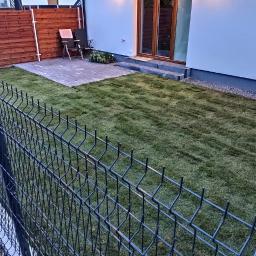 Usługi ogrodnicze Robert Starosz - Świeżo ułożona trawa z rolki w ogrodzie za nowoczesnym domem, widok przez metalowe ogrodzenie panelowe.