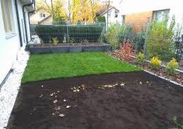 Fragment ogrodu w trakcie zakładania: świeżo rozłożona trawa z rolki sąsiaduje z przygotowaną glebą, w tle widoczne obrzeża rabaty i ogrodzenie.