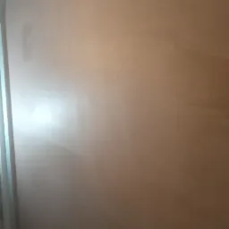 Świeżo nałożona, gładka, brązowa warstwa na ścianie, z widocznym odbiciem światła i fragmentem ościeżnicy po lewej stronie.